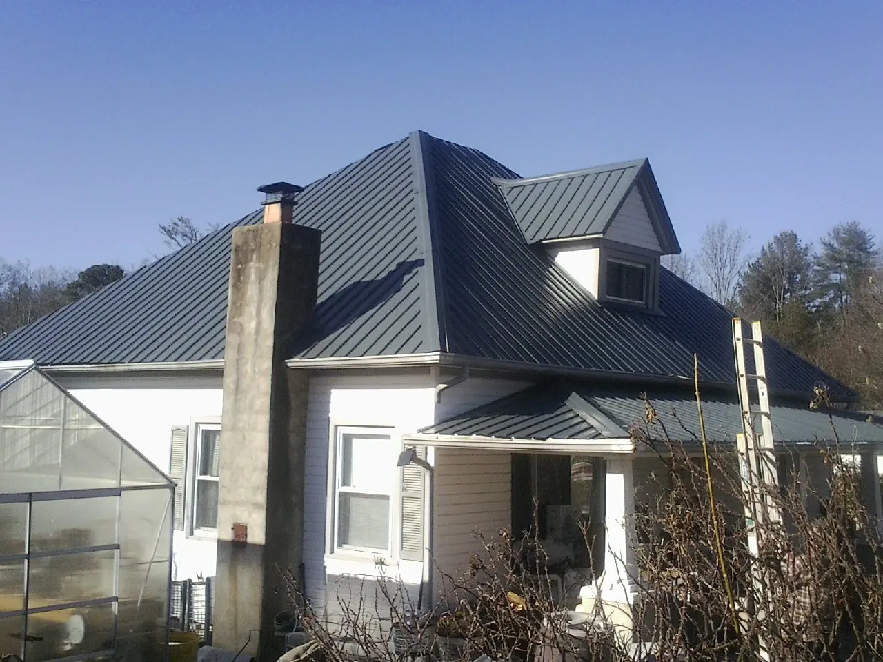 Dark blue standing seam metal roof on a white farmhouse with dormer — Slate & Tile Roof Repair by Roofing Brothers in Frisco