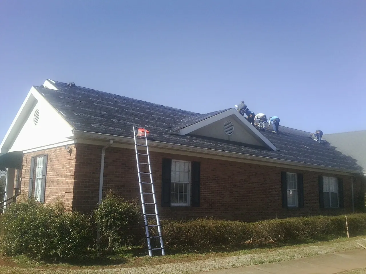Crew tearing shingles off a brick ranch roof with a ladder set — Metal Roof Repair work by our crew in Frisco