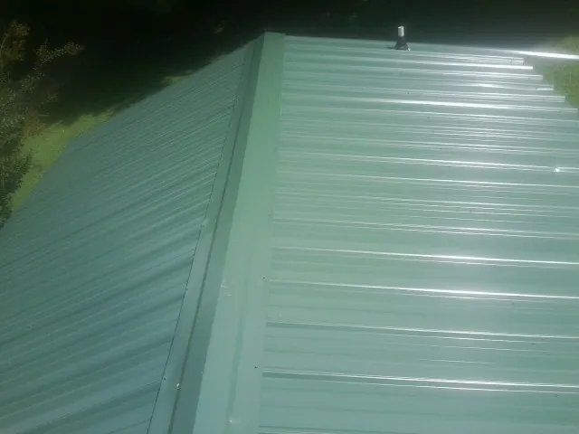 New green metal panels meeting at the ridge of a roof — Flat Roof Repair work by our crew in Frisco